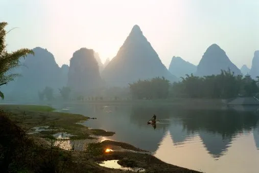 Misty mountains reflected in a quiet river at sunrise